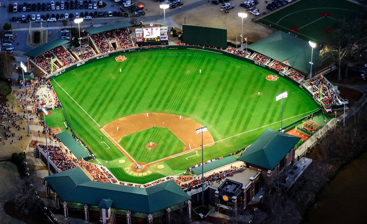 Aerial view of a baseball stadium at night with a game in progress, seated spectators, and illuminated field.