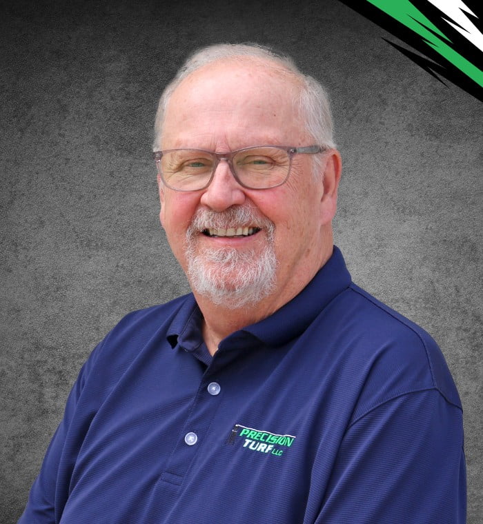 An elderly man with glasses and a beard smiles, wearing a navy blue polo shirt with a logo that reads "Precision Turf." The background is a gray textured surface with green and white accents.