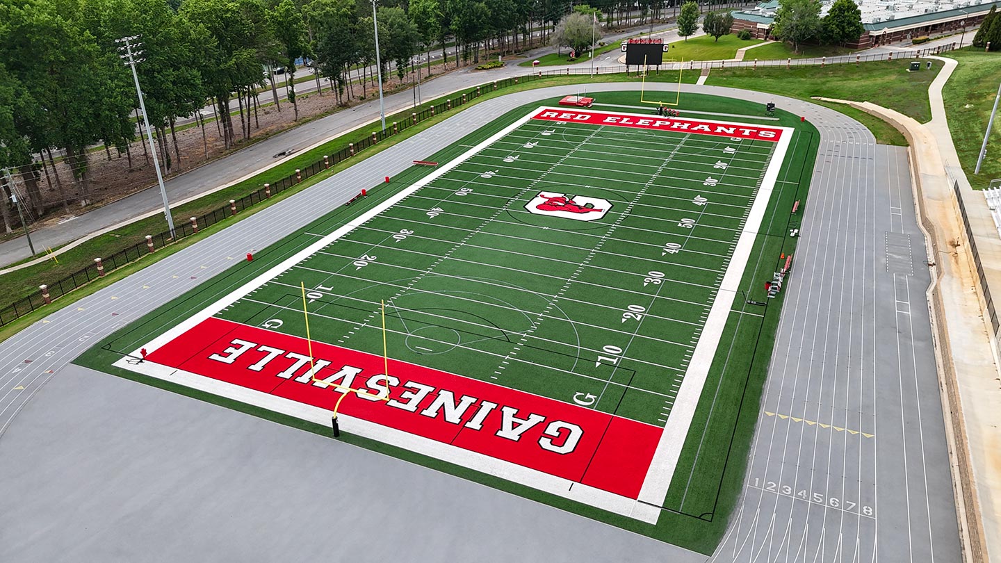 A high school football field with "Gainesville" and "Red Elephants" written on its synthetic turf, surrounded by a running track and trees in the background.