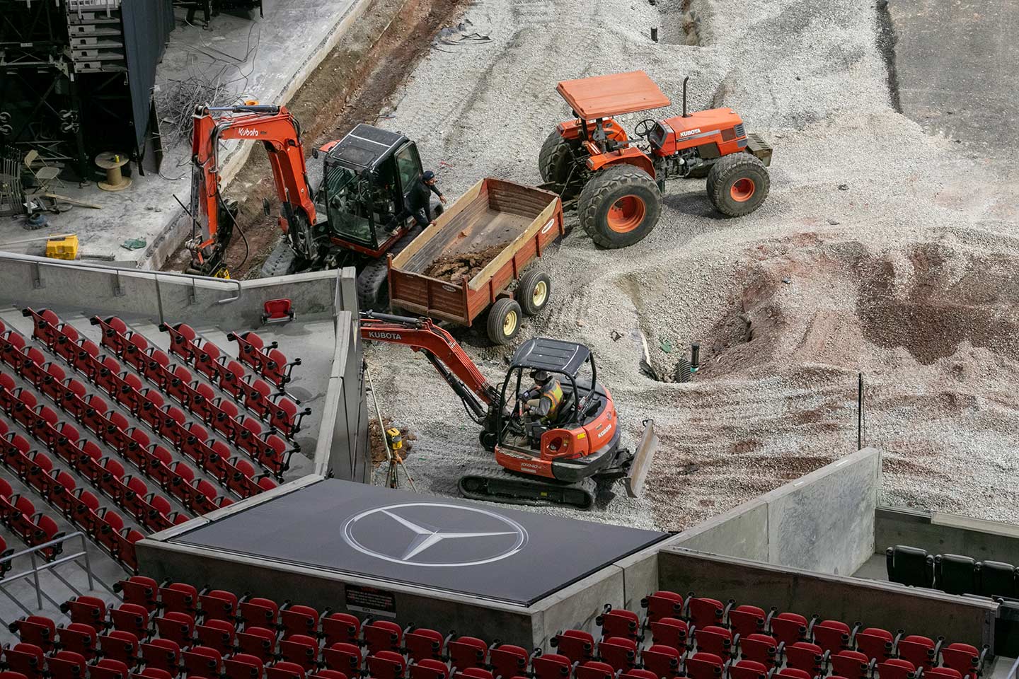 Construction equipment focused on precision turf installation works diligently on the floor of a stadium surrounded by rows of red seats.